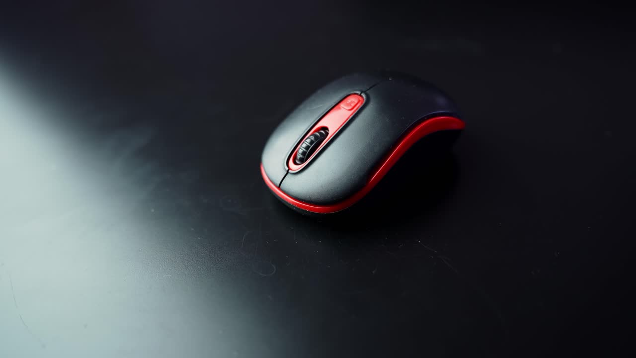 Close-up of black and red wireless computer mouse on dark tabletop with shallow depth of field and copy space, perfect for office, tech, and productivity b-roll