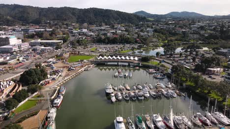 drone fly over docked boats in hatea river, tilt up whangarei cityscape, new zealand