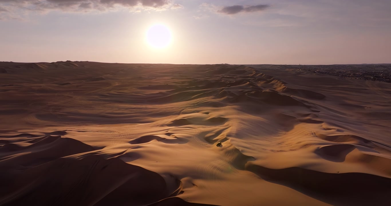 Buggy fuoristrada che attraversa le dune di sabbia vicino a Huacachina, Perù, al tramonto, mostrando un vasto paesaggio desertico e tracce di veicoli nella sabbia, vedute aeree cinematografiche