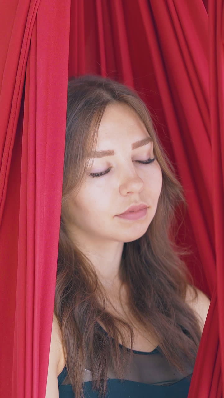 pretty young woman sits relaxed in fly yoga hammock with closed eyes and meditates in modern gym close view
