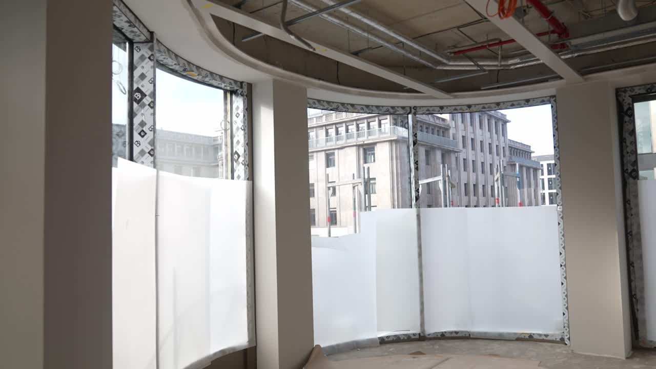 Interior curvo con grandes ventanales en edificio sin terminar, espacio de arquitectura moderna con vistas a la ciudad, fase de renovación con estructura abierta y luz natural en el interior
