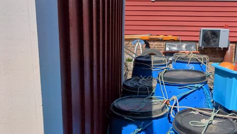 4k 60fps blue plastic drums used as well boxes stored on fishing harbor next to fishing sheds - panning shot