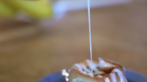 drizzling icing over a freshly baked cinnamon roll - slow motion dripping sticky treat