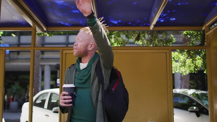 Happy albino african american man with dreadlocks holding takeaway coffee and waving