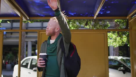 happy albino african american man with dreadlocks holding takeaway coffee and waving