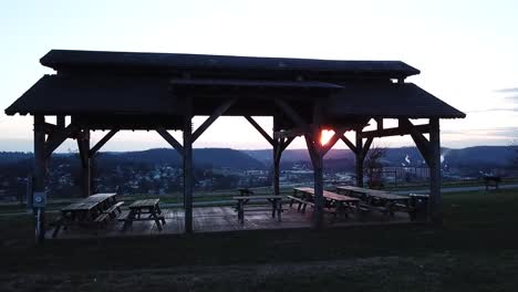 Slow-moving-dolly-shot-pushing-through-a-pavilion-in-Cove-Spring-Park-in-Frankfort,-Kentucky-revealing-a-bourbon-distillery-in-the-background-at-sunset