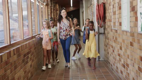 diverse female teacher with schoolgirls walking at elementary school corridor in slow motion