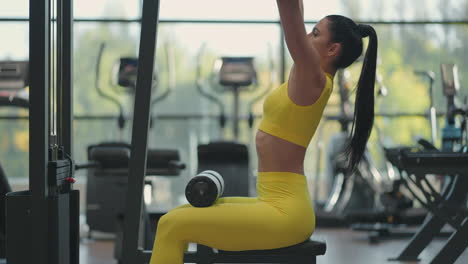 mujer hispana sentada en un simulador en el gimnasio tira de una cuerda de metal con el peso bombea los músculos de la espalda. mujer morena tira del simulador. realizando ejercicio para los músculos de la espalda simulador