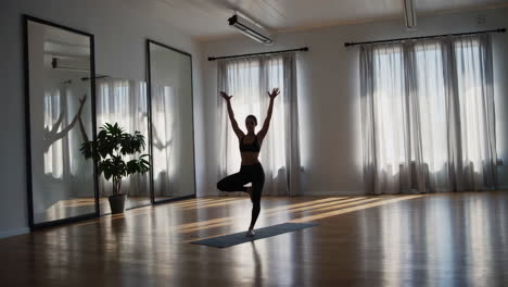 woman practicing yoga tree pose in a sunlit studio