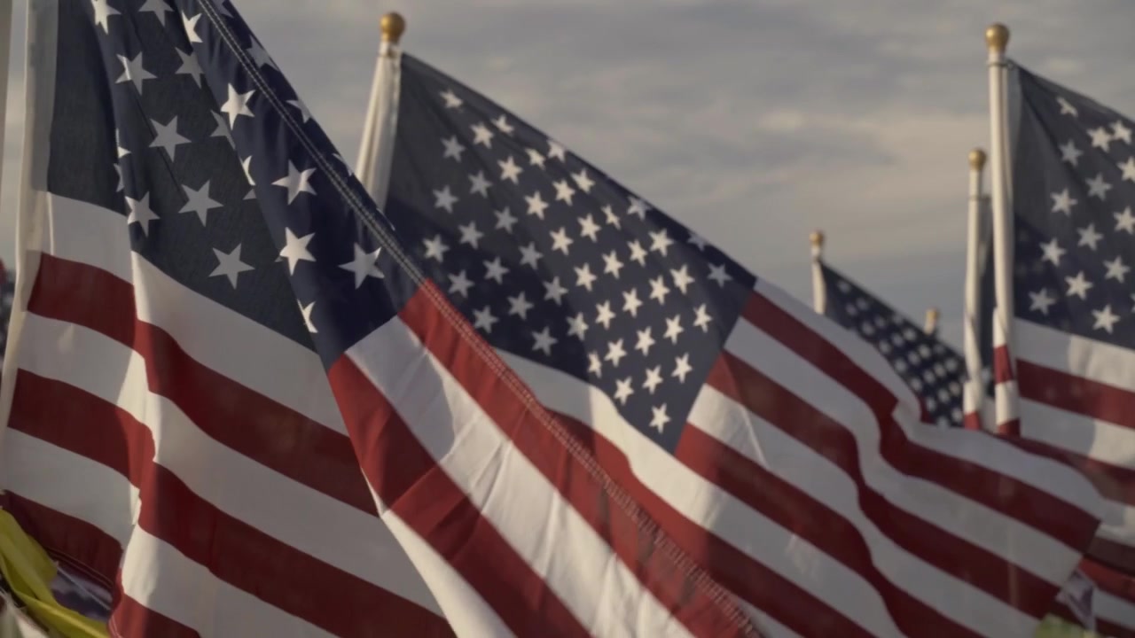 File di bandiere americane sventolano al vento in un sito commemorativo all'aperto dedicato alle vittime dell'11 settembre. Questa scena toccante cattura un tributo patriottico e un solenne ricordo nazionale