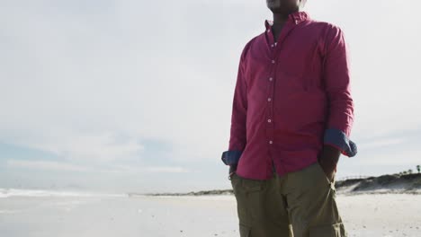 Afroamerikanischer-Mann,-Der-Gedankenverloren-Am-Strand-Spaziert-Und-Auf-Das-Meer-Blickt