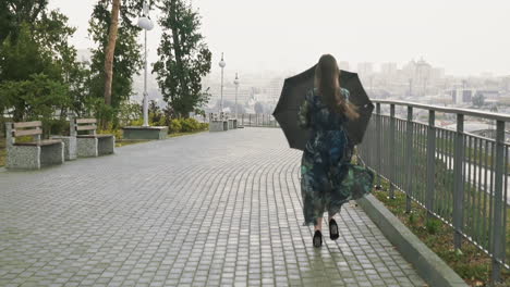 mujer feliz en vestido elegante con paraguas corre a lo largo del parque