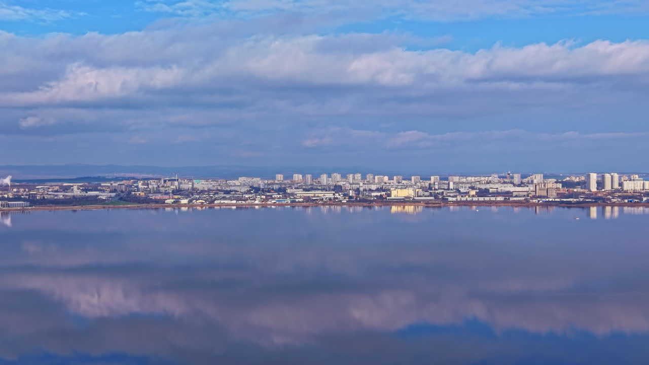 澄み切った空の真昼、穏やかな水面に映る都市のスカイラインと雲