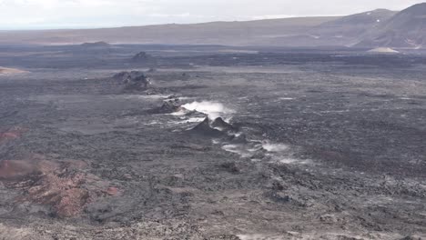 aerial view of a volcanic fissure emitting white steam in a barren, dark lava field in iceland.