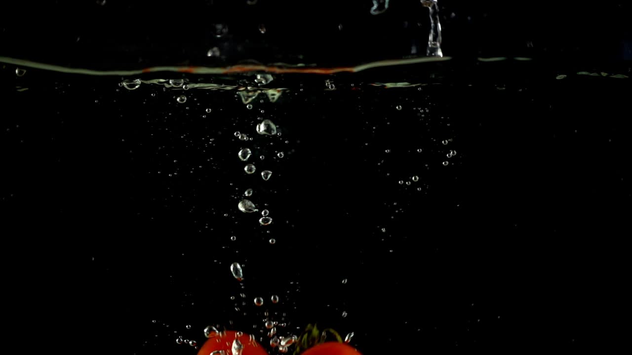 Cherry tomatoes fall in water. Slow motion
