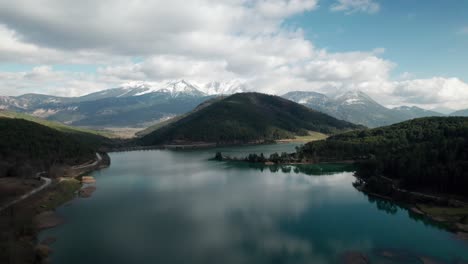 Drone-Aéreo-Sobre-El-Lago-Doxa-Grecia-Nubes-Cinematográficas-Se-Refleja-En-El-Agua-Rodeada-De-Bosques-De-Pinos,-Paisaje-De-Ensueño,-Construcción-Artificial