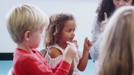 Infant-school-children-in-class-raising-hands,-learning-to-count-with-female-teacher,-side-view