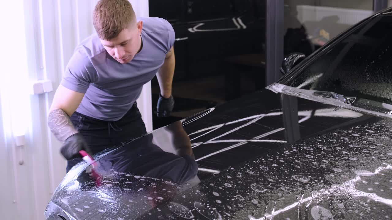 hombre que cubre el coche con cinta de poliuretano de vinilo. películas para el coche. pegatina película protectora en el coche