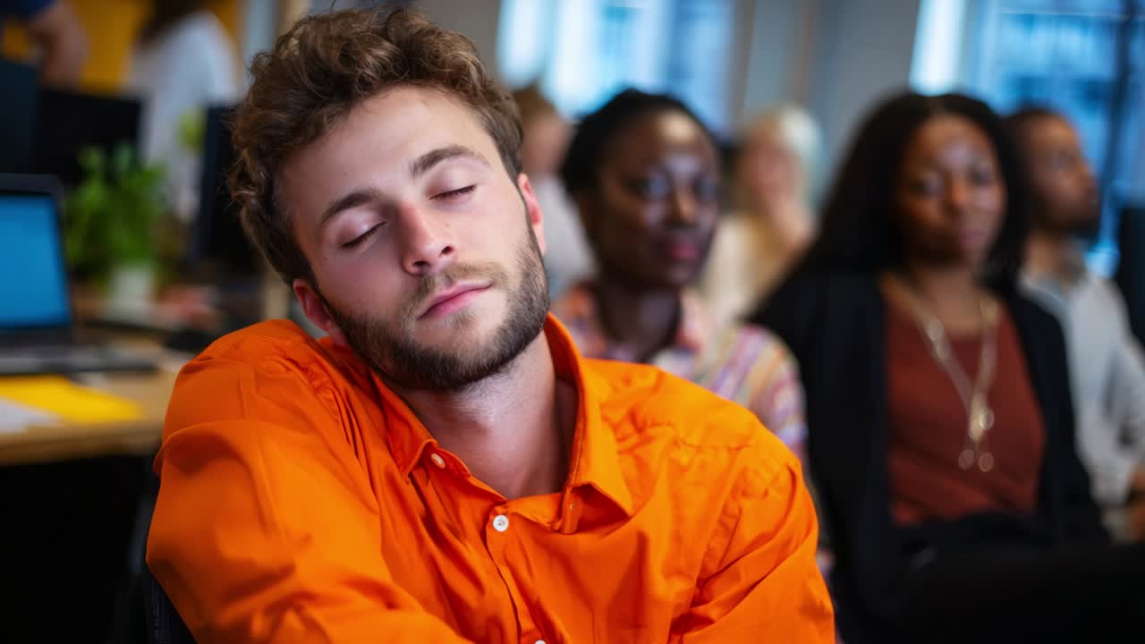 A Young Man in an Orange Shirt Appears to Be dozing Off During a Meeting or Presentation Surrounded by Attentive Colleagues in a Modern Office Setting, Highlighting the Challenges of Maintaining Focus