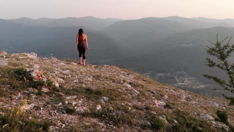 a young woman stands on the edge of a rock and raises her hands.