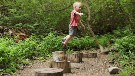 active little blonde child boy playing jumping from wooden logs