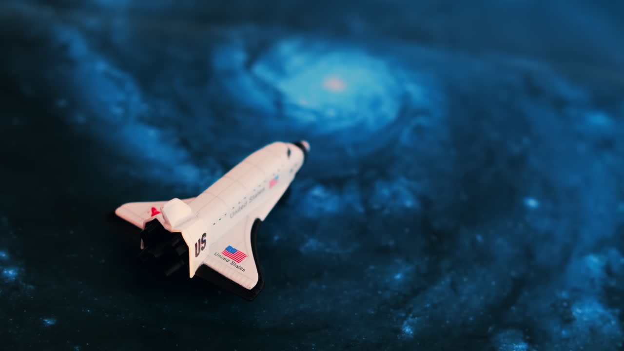 Close up of a miniature toy space shuttle placed on a blue cosmic galaxy backdrop