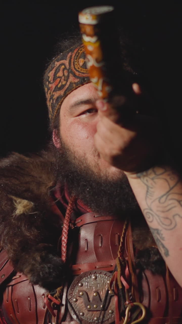 Obese man in ethnic leather costume with fur smokes shaman pipe on dark background slow motion. Folk magic rituals and worship. Hallucinogen tobacco