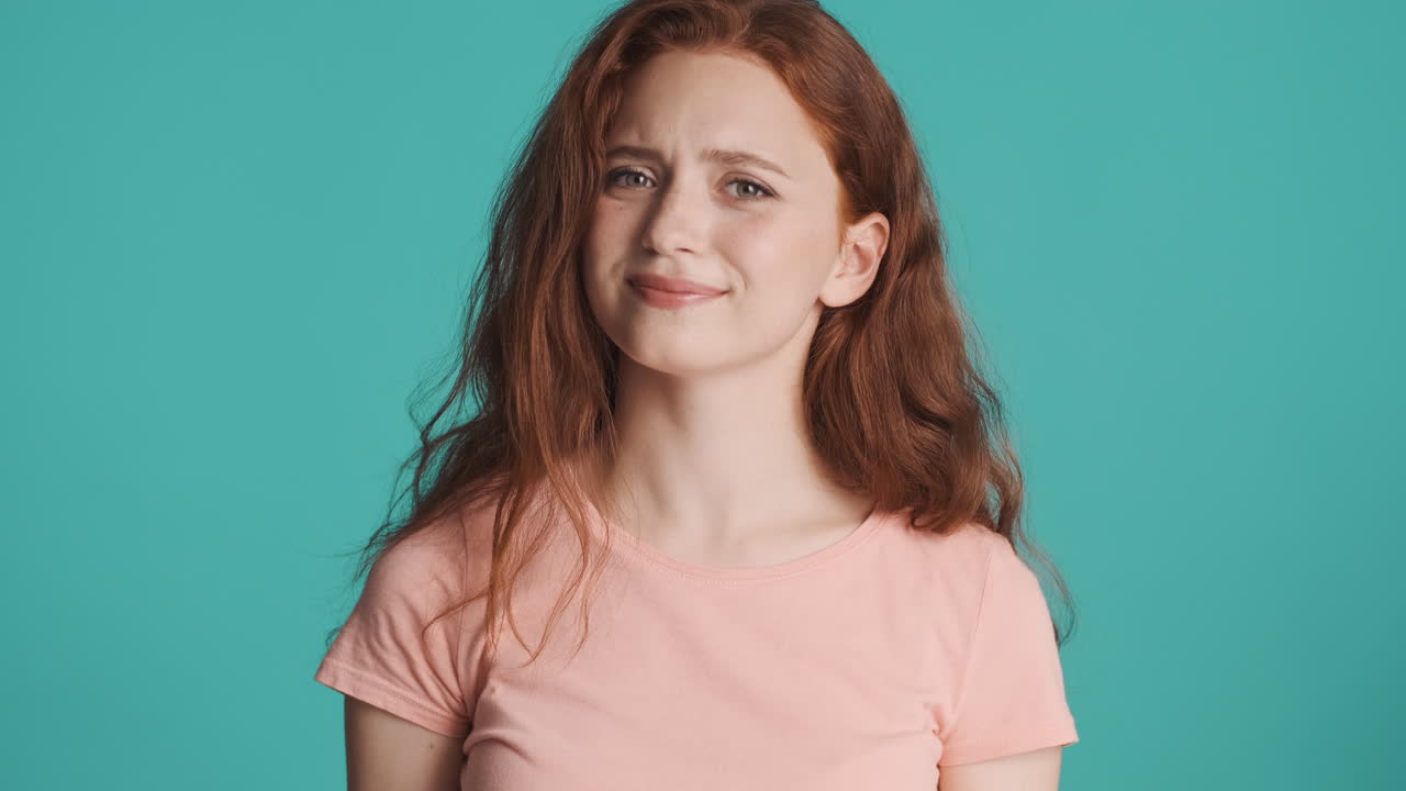 은 머리의 소녀가 르키즈색 배경에서 카메라를 보고 있습니다.