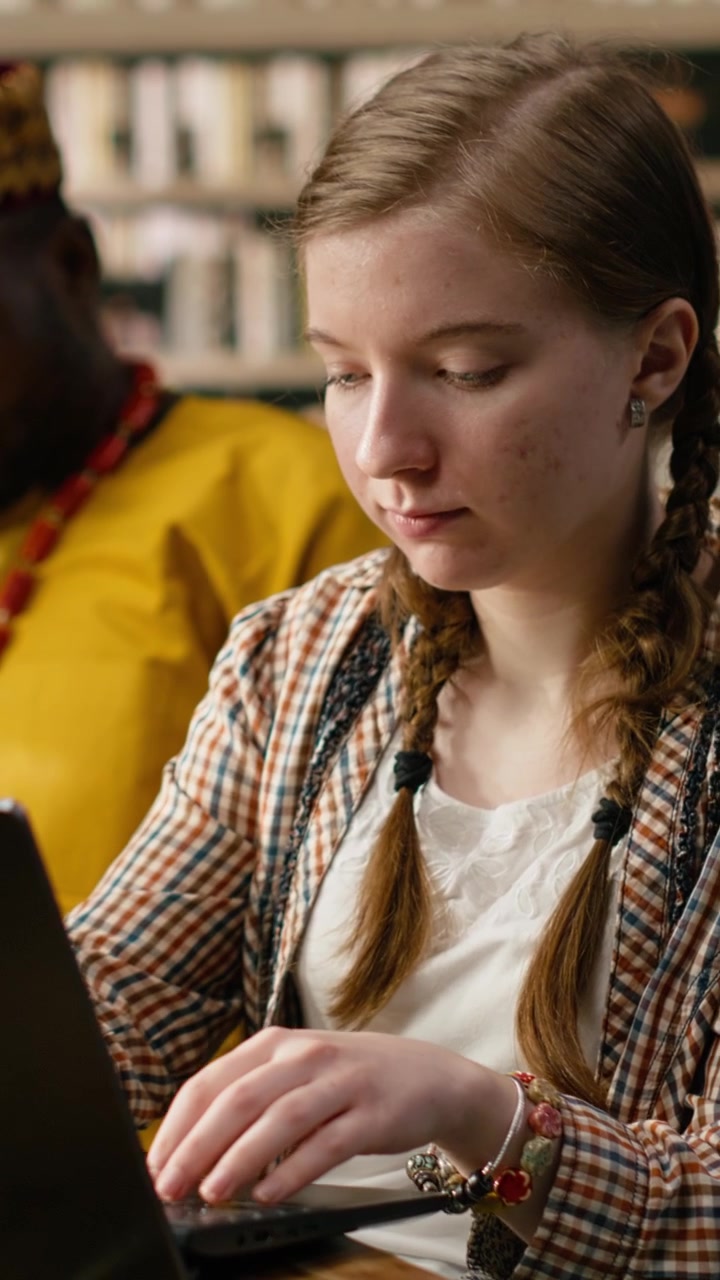 Vertical Video Student Typing On Laptop And Taking Notes Beside Open Book At Busy Study Table