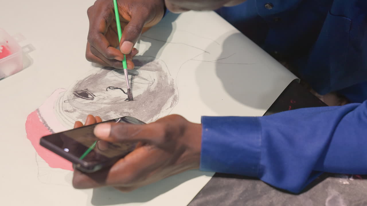 Black artist painting portrait, hands hold phone reference and brush over grayscale sketch, closeup of wrist and fingertip, studio tabletop with palette, slow meditative strokes and focused craft
