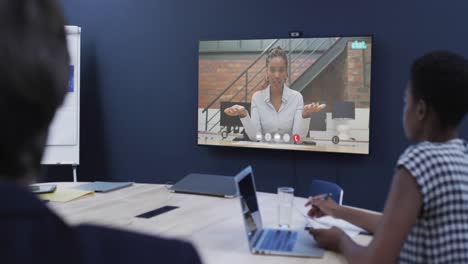 gente de negocios en videoconferencia con una colega afroamericana en la pantalla de televisión
