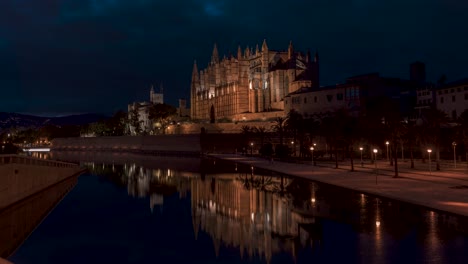 night timelapse view of la seu cathedral ( palma, mallorca, spain). majestic la seu cathedral illuminated against a deep blue night sky. soft water reflections and warm streetlights.