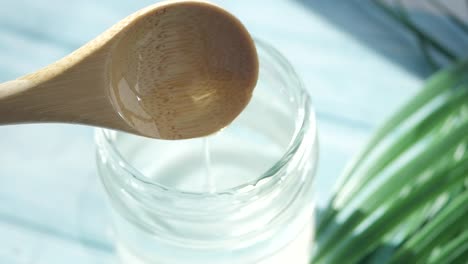 pouring coconut oil from a wooden spoon into a glass jar