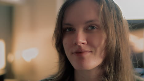 cinematic close up shot of a beautiful white woman's face in her apartment looking around and then staring straight into the camera and smiling during a golden hour sunrise in slow motion