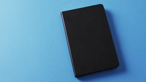 primer plano de un libro negro cerrado con espacio de copia en un fondo azul en cámara lenta