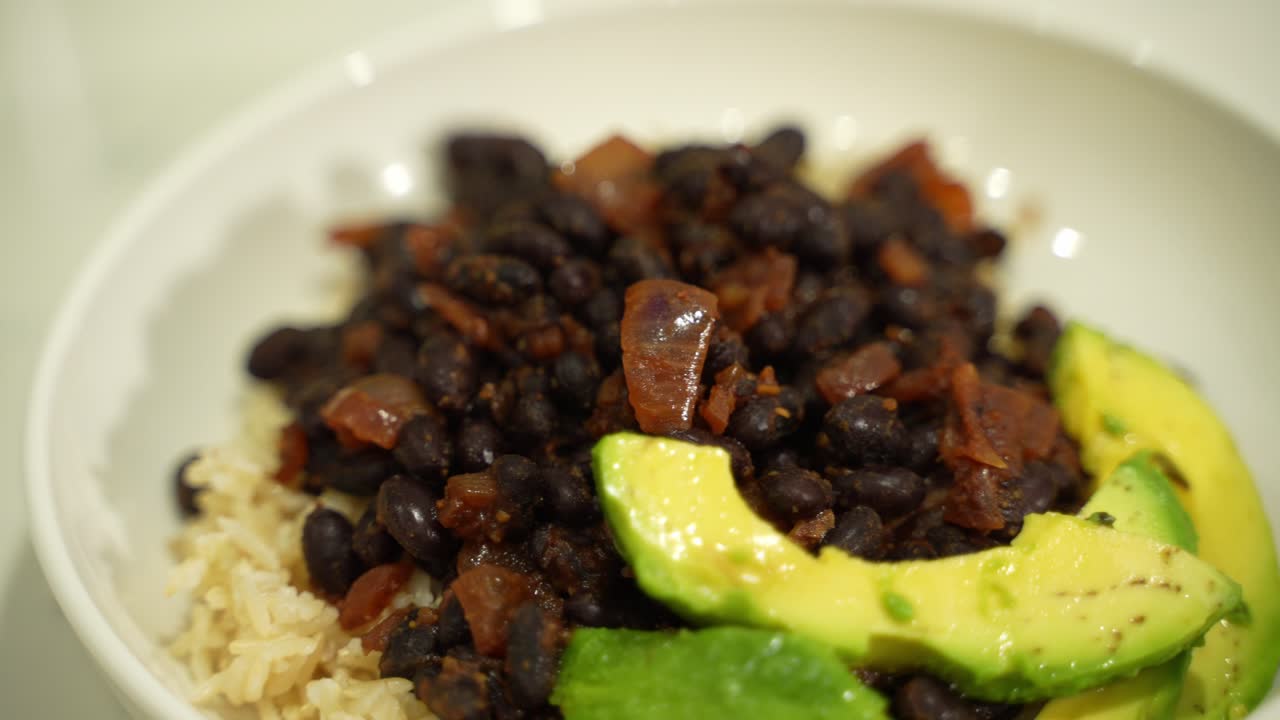 Closeup of rice topped with bean and onion mix and avocado slices in a bowl