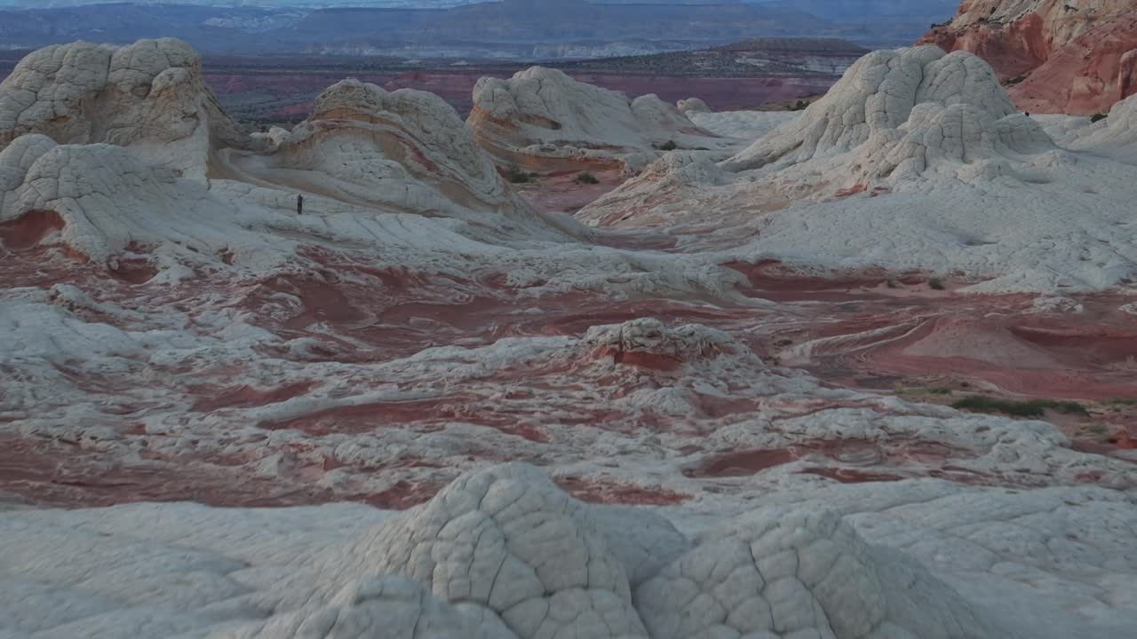 A drone flying backwards and panning up to reveal the unique sandstone features of White Pocket Arizona surrounded by the sandy desert of the Vermillion Cliffs at blue hour sunrise