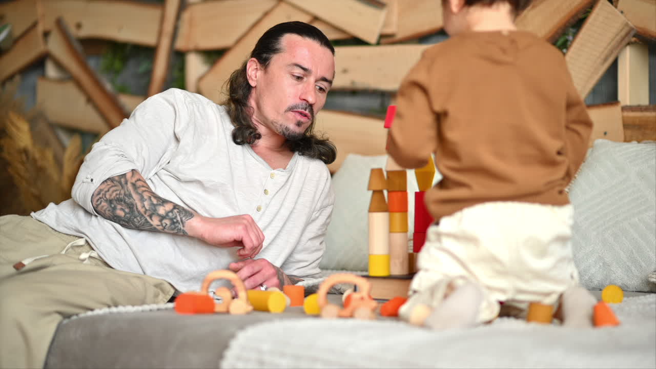 Father playing with his son with colourful, ecological wooden toys on the bed