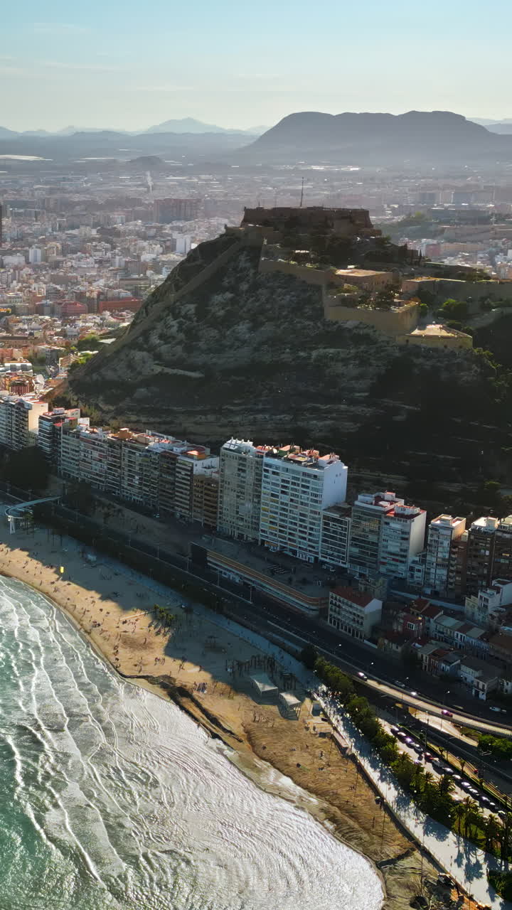 Luftdronebillede af Santa Barbara-slottet ved kysten af Alicante, Spanien med byen og havet i dagslys. Lodret