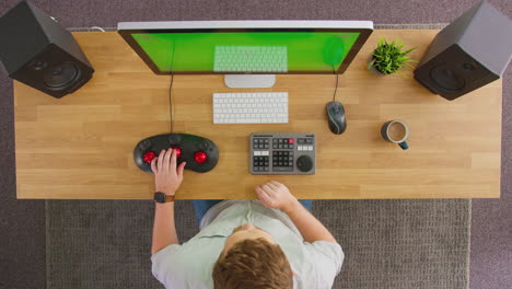 overhead view of male video editor working at computer with green screen in creative office