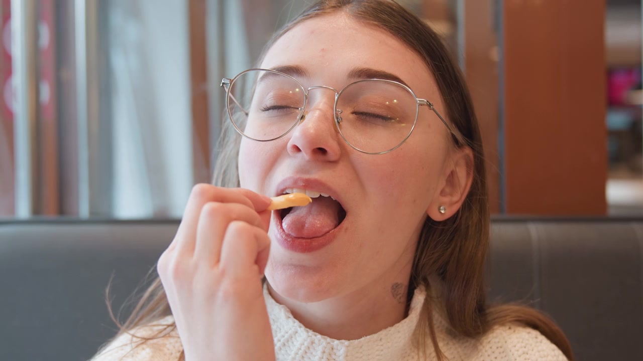 Gros plan d'une jeune femme examinant une petite capsule près de son œil, portant sa main à sa bouche pour prendre une pilule, puis se détendant avec un bref sourire dans une cabine intérieure chaleureuse, avec une lumière naturelle douce et une ambiance décontractée.