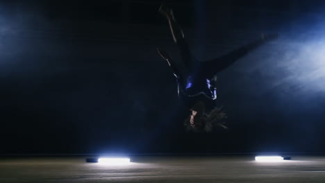 a girl performs a jump gymnastics on a dark background in the smoke