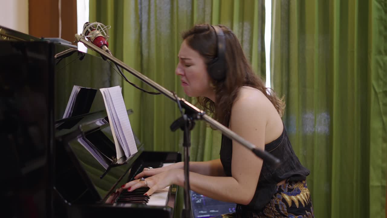 Woman playing piano and singing in a recording studio