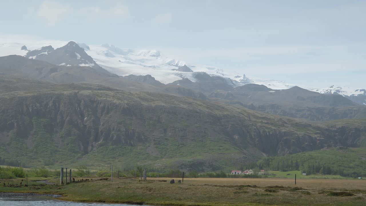 montañas cubiertas de nieve en el campo islandés con un lago y casas en primer plano