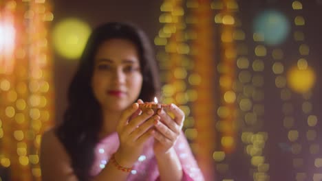 woman celebrating festival of diwali holding lit diya oil lamp towards camera