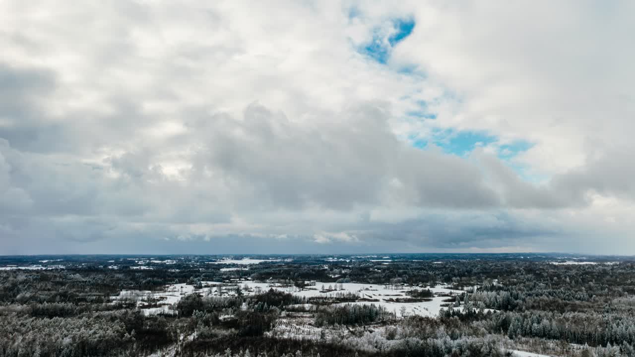 Aerial winter hyperlapse in countryside with snow covered forest and moving clouds.