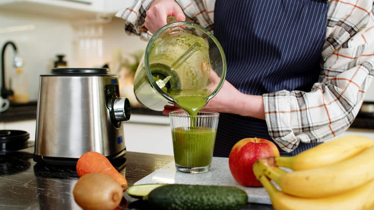 Donna versa un frullato nel bicchiere dopo aver frullato spinaci, banana, mela, carota, una bevanda salutare in cucina