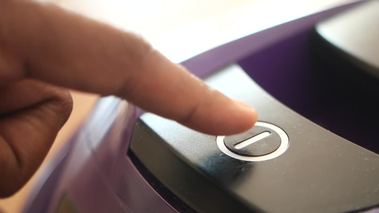 una mano presiona el botón de encendido en un dispositivo púrpura