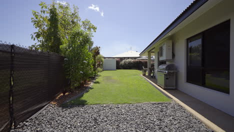 lado de la casa que conduce al césped moderno del patio trasero, áreas de entretenimiento al aire libre y una lujosa piscina en el suelo con bordes de concreto