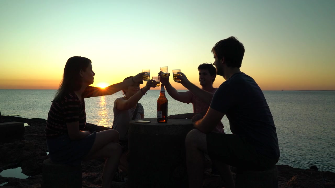 Sagome di amici che brindano con birra in spiaggia al tramonto